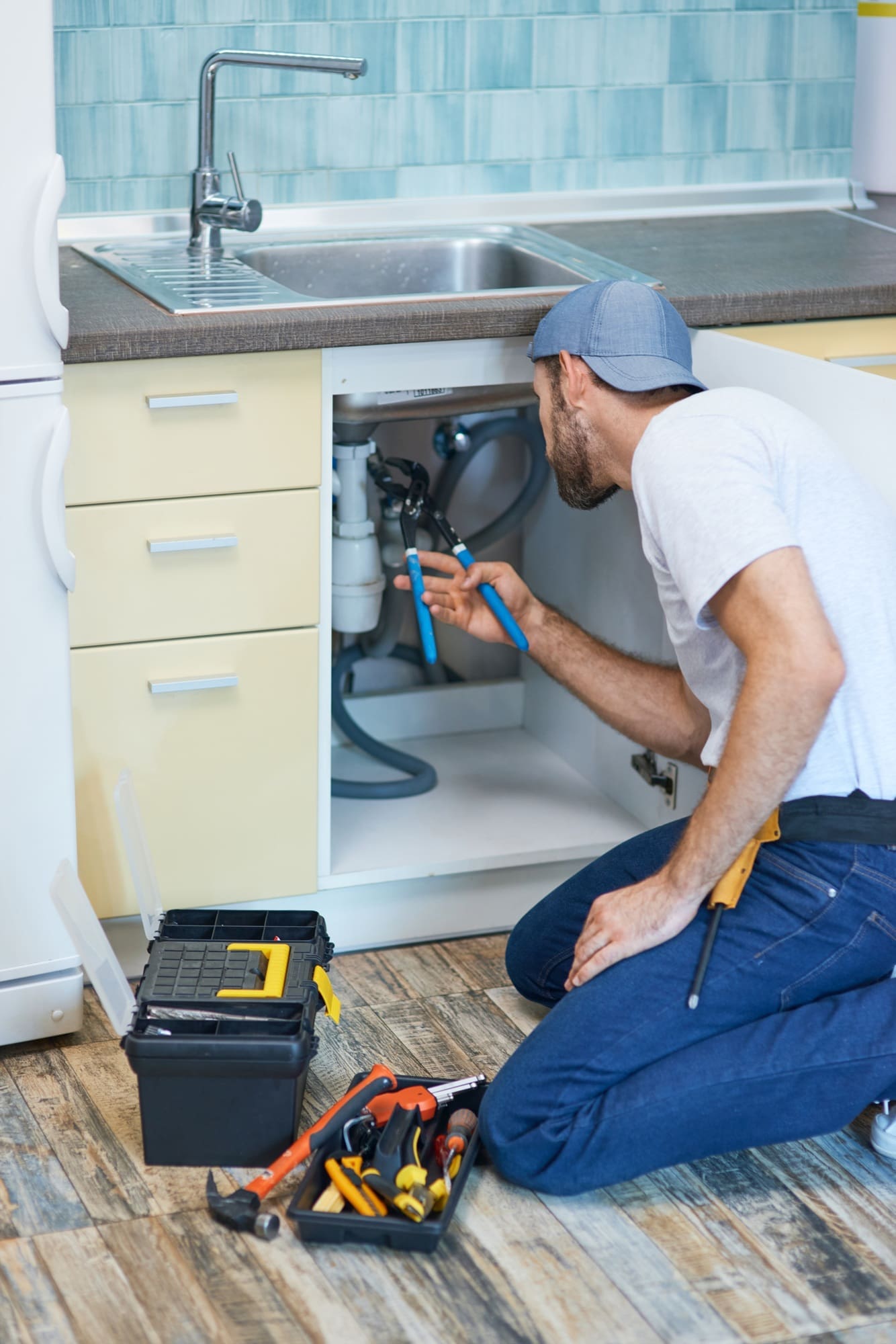 Plumbing troubles. Professional plumber using pipe wrench while examining and fixing sink pipe in